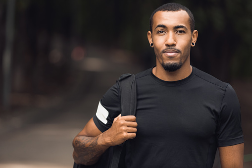 Muscular african-american man wearing black t-shirt and backpack posing outside after workout