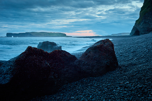 Icelandic coastline. Sun shining above black beach and cliffs