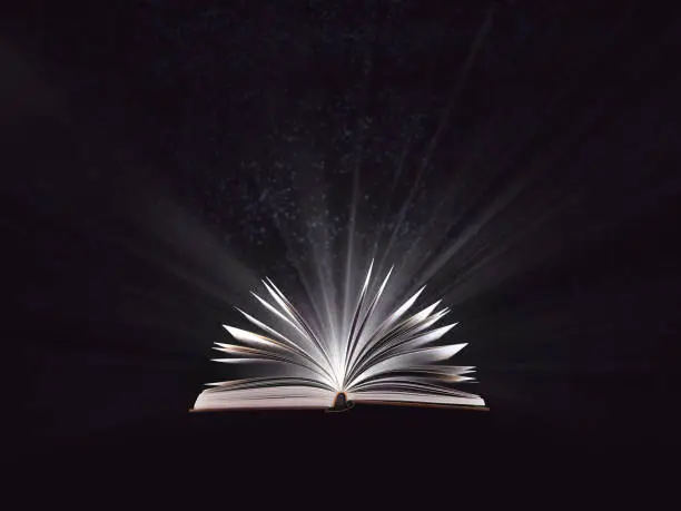 Photo of An open magic book, bewitched book glows in the darkness, magic light. Education. Dreamy image of a fairytale