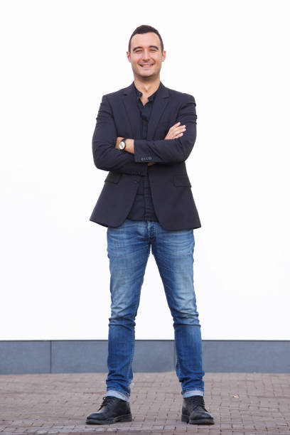 istock Full body confident man standing against white wall with blazer and jeans 1084132016