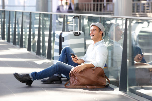 istock happy man sitting on floor with suitcase bag and cellphone 1084132074