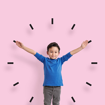 6-7 years old child standing in front of pink wall. His arms are open like clock.