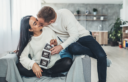 Happy pregnant woman with baby ultrasound photo embracing with her husband