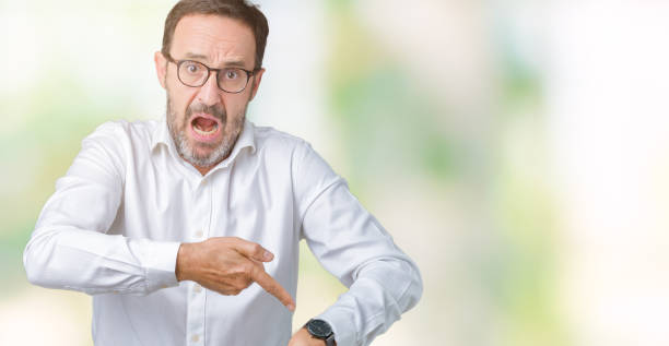 handsome middle age elegant senior business man wearing glasses over isolated background in hurry pointing to watch time, impatience, upset and angry for deadline delay - clock face clock deadline human hand imagens e fotografias de stock