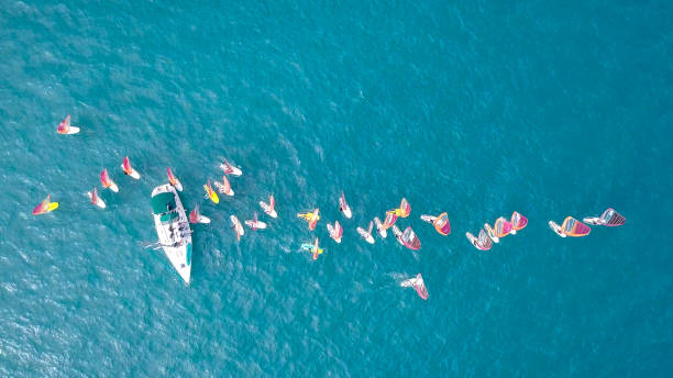istock Small white yacht surrounded by a large group of Wind surfers 1084170668