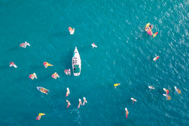 istock Small white yacht surrounded by a large group of Wind surfers 1084170826