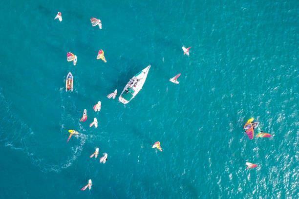 istock Small white yacht surrounded by a large group of Wind surfers 1084171022