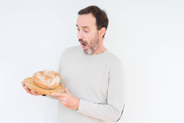 istock Senior man holding homemade fresh bread over isolated background scared in shock with a surprise face, afraid and excited with fear expression 1084171508