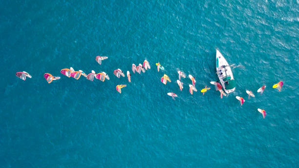 istock Small white yacht surrounded by a large group of Wind surfers 1084171558
