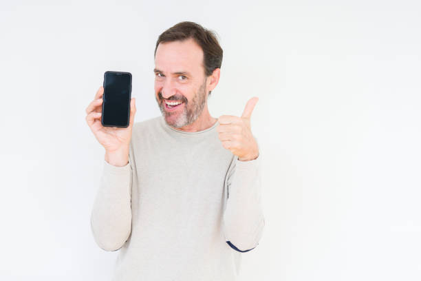 istock Senior man showing smartphone screen over isolated background happy with big smile doing ok sign, thumb up with fingers, excellent sign 1084171576