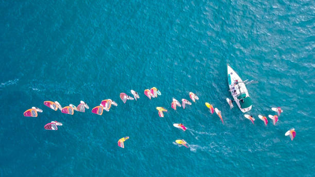 istock Small white yacht surrounded by a large group of Wind surfers 1084171698