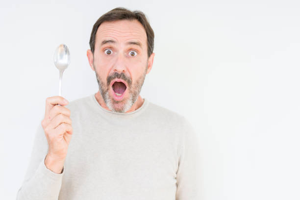 istock Senior man holding silver spoon over isolated background scared in shock with a surprise face, afraid and excited with fear expression 1084171770