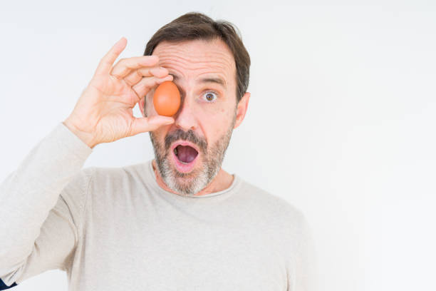 Senior man holding fresh egg over isolated background scared in shock with a surprise face, afraid and excited with fear expression