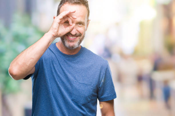 istock Middle age hoary senior man over isolated background doing ok gesture with hand smiling, eye looking through fingers with happy face. 1084174266
