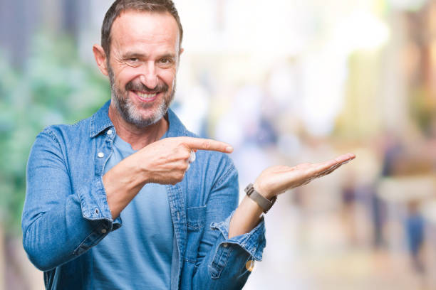 istock Middle age hoary senior man over isolated background amazed and smiling to the camera while presenting with hand and pointing with finger. 1084174330