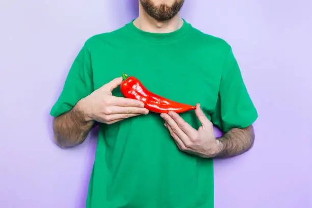 Young man holding red capi pepper in his hands on green t-shirt background. Light purple wall on background, copy space.