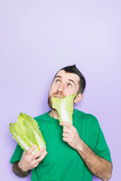 istock Young man biting on a leaf of Beijing napa cabbage 1084210456