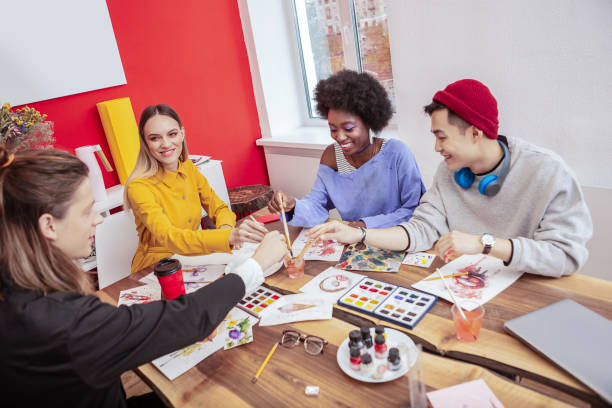 istock Four creative art students painting on white sheets of paper 1084217684