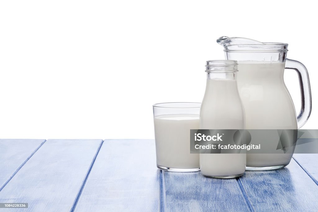 Milk jar, milk bottle and milk glass shot on blue striped table against blue striped table Milk jar, milk bottle and milk glass shot on blue striped table against white background. Suitable for digital replacement of the white background with any image. The composition is at the right of an horizontal frame leaving useful copy space for text and/or logo. Predominant colors are white and blue. High key DSRL studio photo taken with Canon EOS 5D Mk II and Canon EF 100mm f/2.8L Macro IS USM. Milk Stock Photo