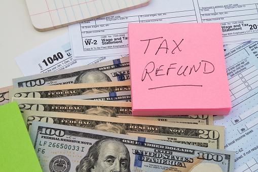 An IRS tax return form 1040 and a W-2 Wage and Tax Statement forms with US currency and a reminder note saying Tax Refund.