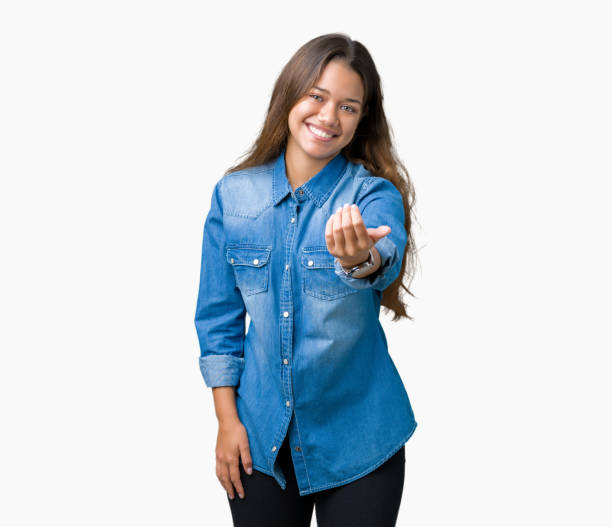 młoda piękna brunetka kobieta ubrana w niebieską dżinsową koszulę na odizolowanym tle beckoning przyjdź tutaj gest z ręką zapraszając szczęśliwy i uśmiechnięty - skinąć zdjęcia i obrazy z banku zdjęć