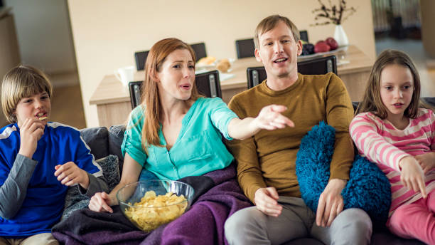 famiglia che guarda la tv mentre fa spuntini con patatine fritte - family sofa potato chip group of people foto e immagini stock