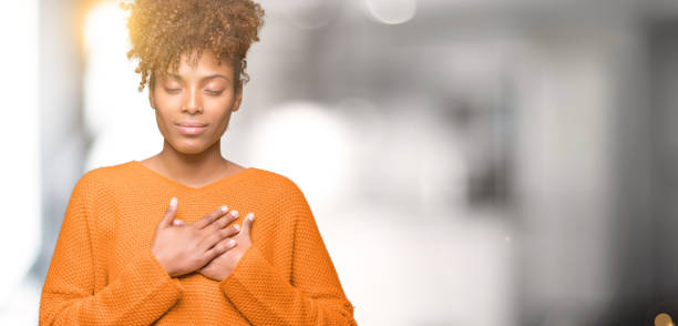 bella giovane donna afroamericana su sfondo isolato sorridente con le mani sul petto con gli occhi chiusi e gesto grato sul viso. concetto di salute. - photography human hand portrait women foto e immagini stock