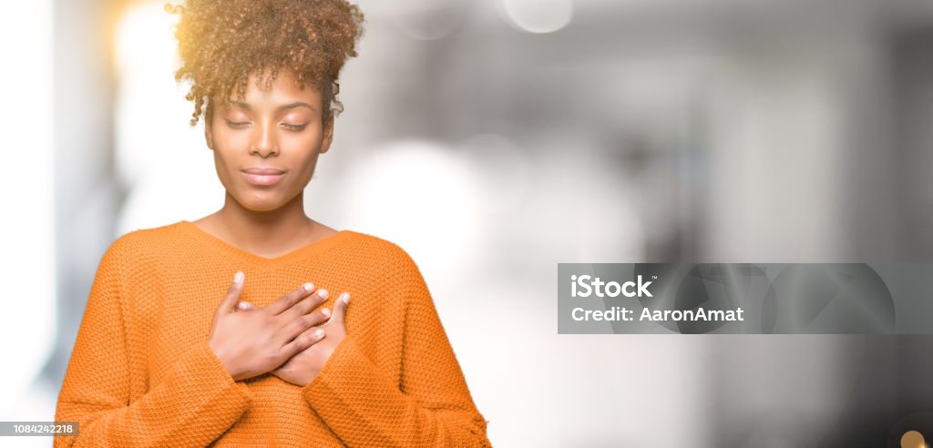 Beautiful young african american woman over isolated background smiling with hands on chest with closed eyes and grateful gesture on face. Health concept. Healthy Lifestyle Stock Photo