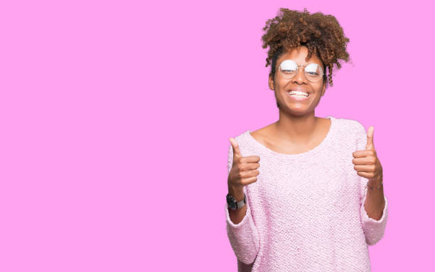 schöne junge afroamerikanische frau mit brille über isolierte hintergrund erfolg zeichen tun positive geste mit der hand, daumen, lächelnd und glücklich. mit fröhlichen ausdruck, gewinner geste schaut in die kamera. - thumbs up african descent teenager women stock-fotos und bilder