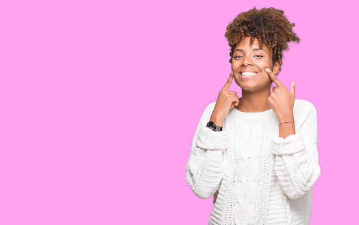 Beautiful young african american woman wearing winter sweater over isolated background Smiling with open mouth, fingers pointing and forcing cheerful smile