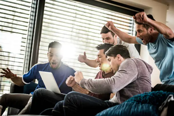 Photo of Excited friends cheering while watching sports match on a laptop