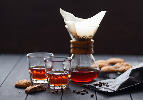 Coffee making gadget. Manual drip brewing filtered coffee in glasses served with cookies on dark background