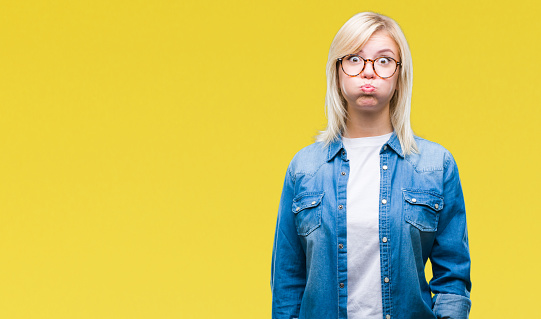 Young beautiful blonde woman wearing glasses over isolated background puffing cheeks with funny face. Mouth inflated with air, crazy expression.