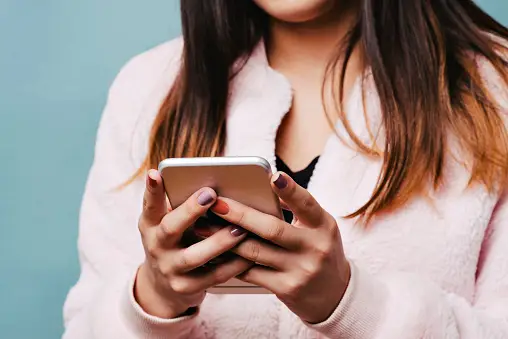 Teen Female Texting on a Smart Phone with Solid Blue Background and Pink Fur Jacket