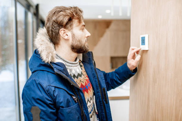 istock Man adjusting temperature with thermostat at home 1084278282