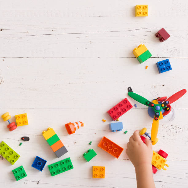 istock Top view on child's hands playing with colorful plastic toy bricks and small details on white wooden table background 1084278580