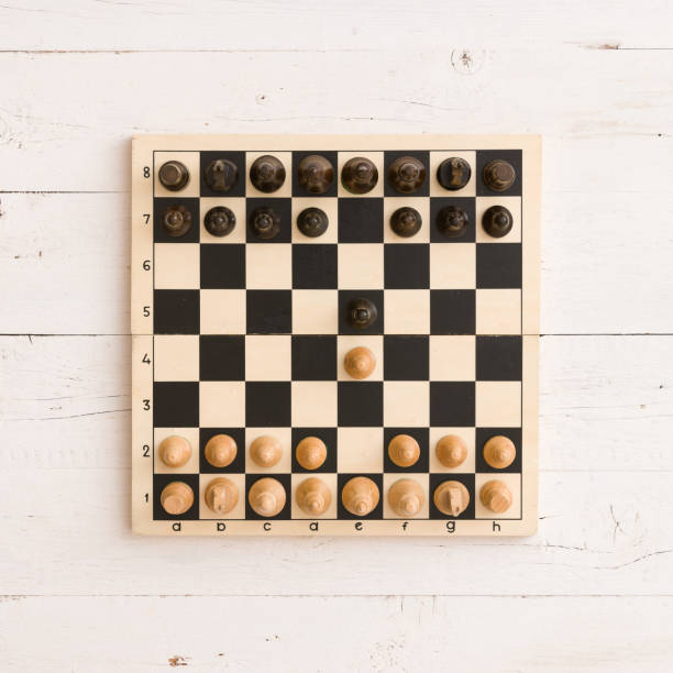 istock Top view on wooden chess board with figures on white wooden table background. First chess move. 1084278604