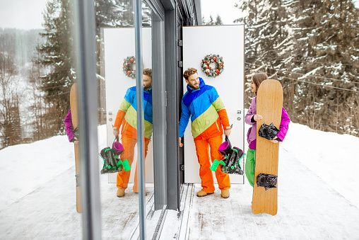 Young couple in coloful ski suits entering home or hotel after snowboarding in the snowy mountains