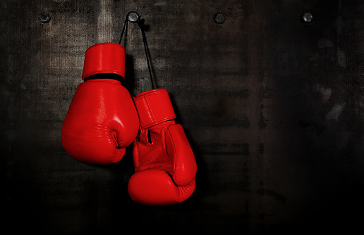 Close up pair of red leather boxing gloves hanging over black wall with copy space