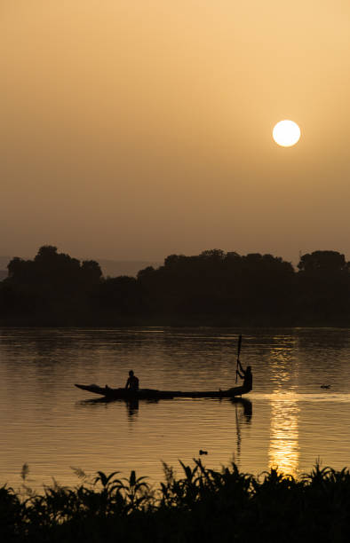 Silhouetted fishermen in canoe on Niger river near Niamey at sunset stock photo
