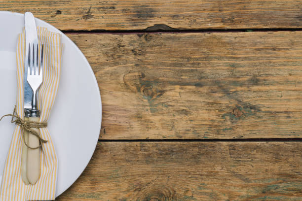 istock Empty white rustic plate on old wooden background with knife, fork and napkin. Rustic food concept. Copy space 1084280724