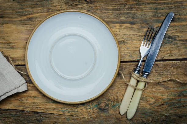 istock Empty white rustic plate on old wooden background with knife, fork and napkin. Rustic food concept. Copy space 1084280744