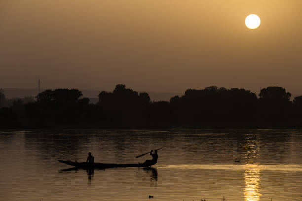 silhouetted fishermen in canoe on niger river near niamey at sunset - niger river imagens e fotografias de stock