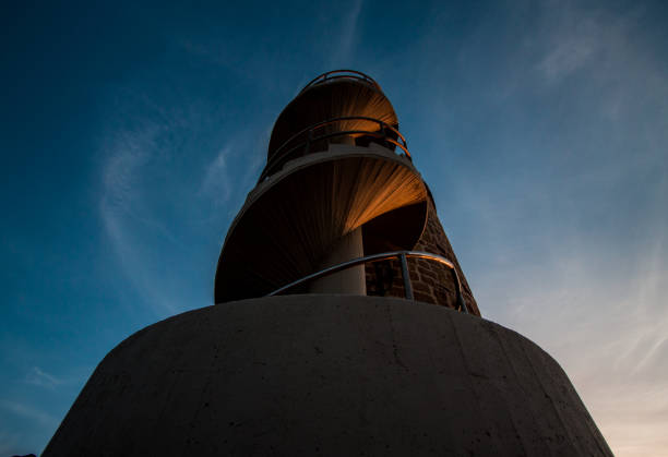 A solitary woman looks over the edge of a railing and into the distance.  The structure she is standing on is a large circular ramp that spirals upward.