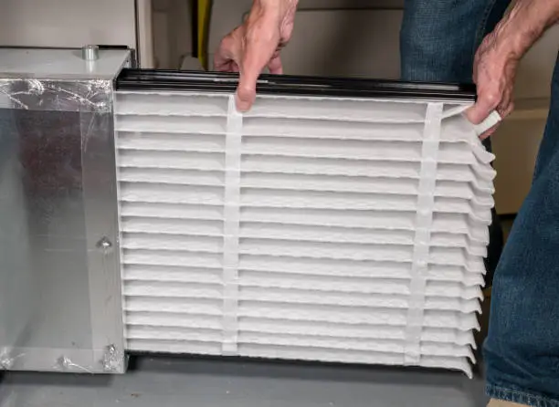 Photo of Senior man inserting a new air filter in a HVAC Furnace