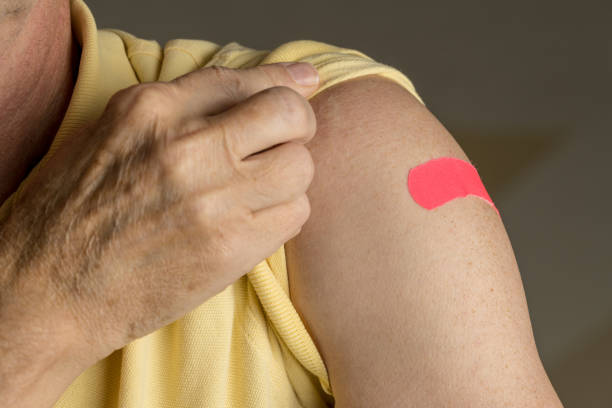 Senior man holding up shirt after flu injection Senior caucasian man holding up shirt sleeve to show the sticking plaster after a flu jab in shoulder adhesive bandage stock pictures, royalty-free photos & images