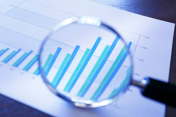 A close up of a magnifying glass rests on top of a bar graph that shows growing sales or increasing performance over a quarterly basis. The image is photographed using a very shallow depth of field.