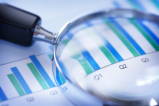 A magnifying glass rests on top of a bar graph that shows increasing sales or performance over a quarterly basis. The image is photographed using a very shallow depth of field.