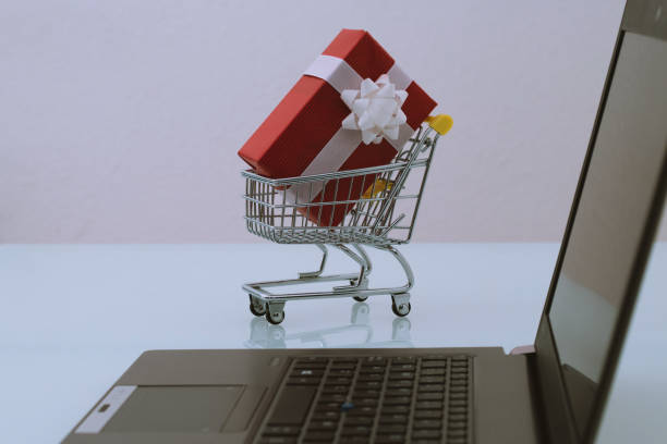 istock Small trolley with a red gift and a black computer. Buy products on an e-commerce in internet. Last minute christmas shopping online concept. 1084314582