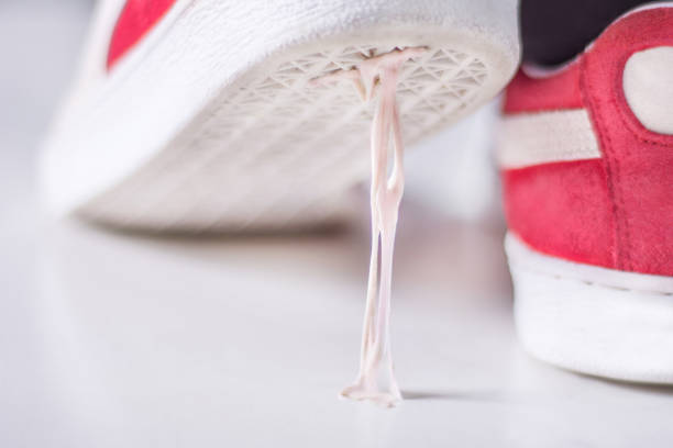 Sneakers stepping in chewing gum on white surface Red sneakers stepping in chewing gum on white surface. Sticky bubble gum on sole of sport footwear. Stickiness concept. Close up, selective focus bubble gum photos stock pictures, royalty-free photos & images